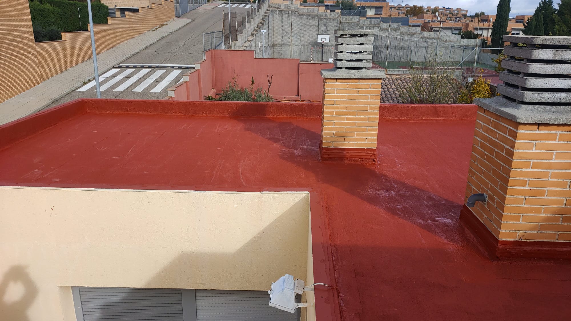 Cubierta plana de gran superficie impermeabilizada en color rojo teja con dos chimeneas de ladrillo, trabajo realizado por Aislamientos de Poliuretano CV