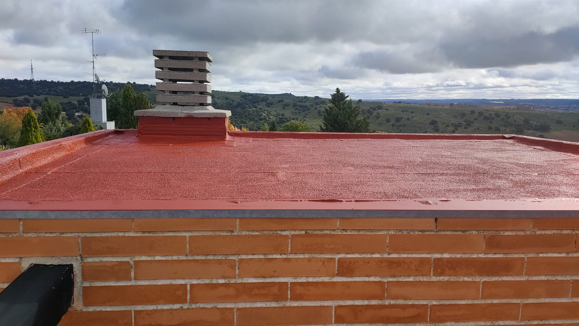 Cubierta plana impermeabilizada con membrana de poliuretano color rojo teja, paisaje rural al fondo, trabajo de Aislamientos de Poliuretano CV