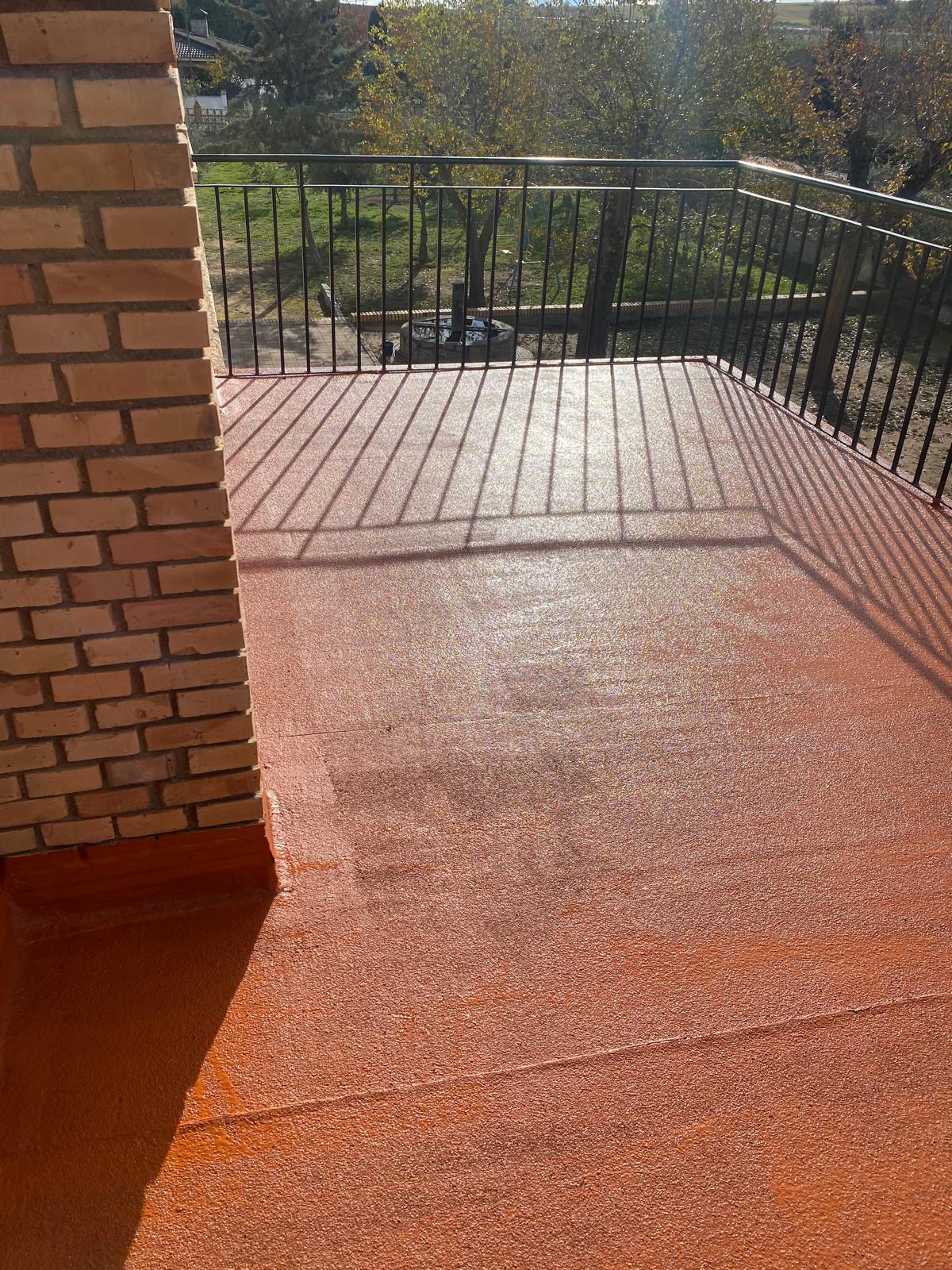 Terraza impermeabilizada con membrana de poliuretano en color naranja y textura antideslizante, con chimenea de ladrillo, ejecutada por Aislamientos de Poliuretano CV