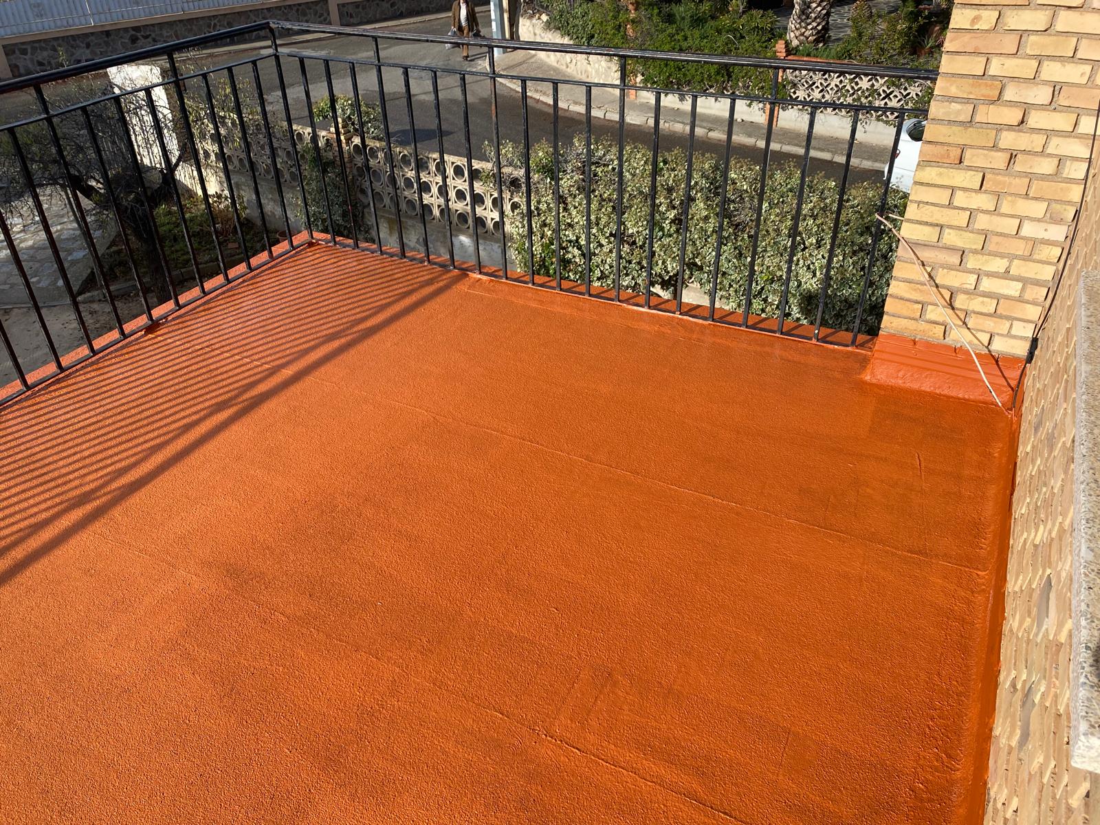 Terraza residencial pequeña impermeabilizada en color naranja con barandilla negra, trabajo de Aislamientos de Poliuretano CV